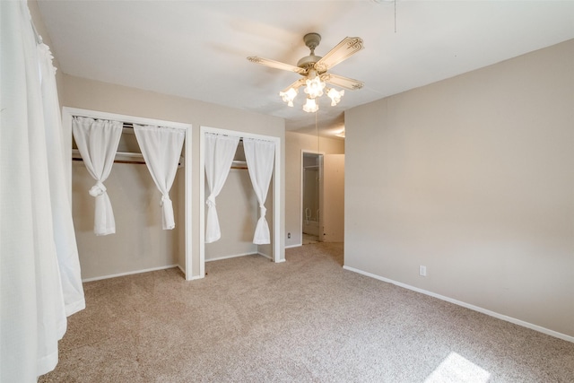 unfurnished bedroom with two closets, light colored carpet, and ceiling fan