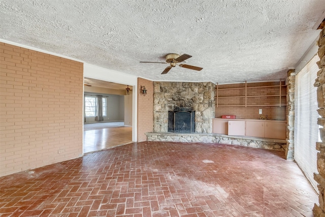 unfurnished living room featuring ceiling fan, brick wall, and a stone fireplace