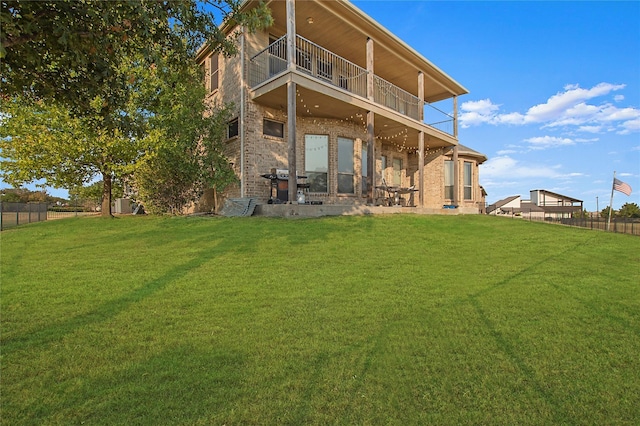 back of house featuring a yard, brick siding, a balcony, and fence