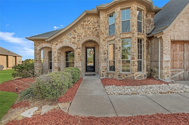 entrance to property with stone siding and roof with shingles