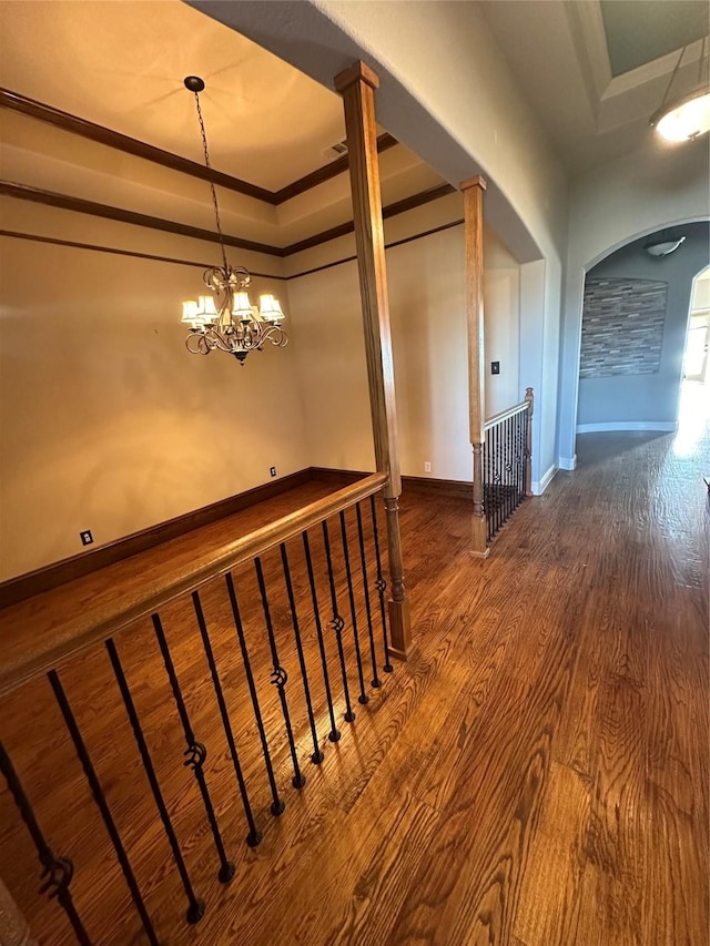 corridor with a tray ceiling, hardwood / wood-style flooring, crown molding, and a chandelier