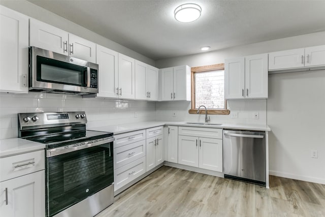 kitchen with light wood-type flooring, appliances with stainless steel finishes, sink, and white cabinets