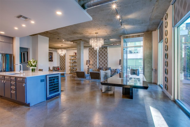 kitchen featuring pendant lighting, sink, a kitchen island with sink, an inviting chandelier, and wine cooler