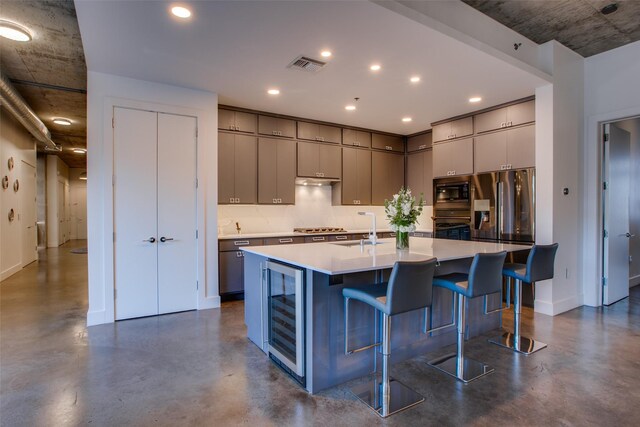 kitchen with wine cooler, a center island with sink, a kitchen breakfast bar, stainless steel appliances, and decorative backsplash