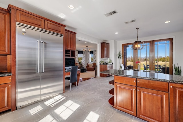 kitchen with built in fridge, decorative light fixtures, an inviting chandelier, and dark stone counters