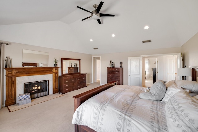 bedroom featuring lofted ceiling, a tiled fireplace, light carpet, and ceiling fan