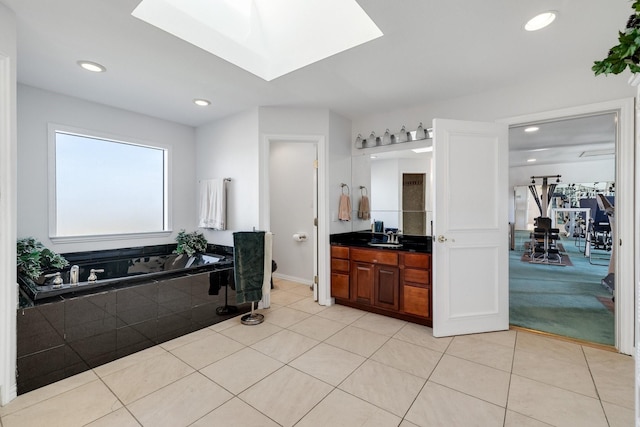 bathroom with tile patterned flooring, vanity, tiled bath, and a skylight