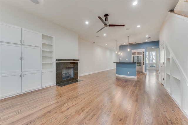 unfurnished living room featuring built in shelves, a tile fireplace, light hardwood / wood-style floors, and ceiling fan