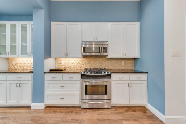 kitchen featuring stainless steel appliances, white cabinets, light wood-type flooring, and dark stone counters