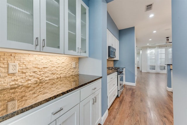 kitchen featuring white cabinetry, light hardwood / wood-style flooring, dark stone counters, stainless steel appliances, and backsplash