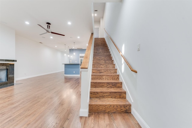 stairs featuring ceiling fan, a tiled fireplace, and hardwood / wood-style floors