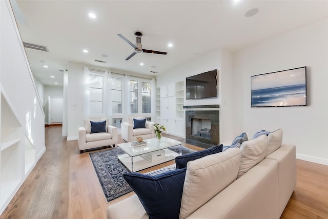 living room featuring built in features, ceiling fan, and light wood-type flooring