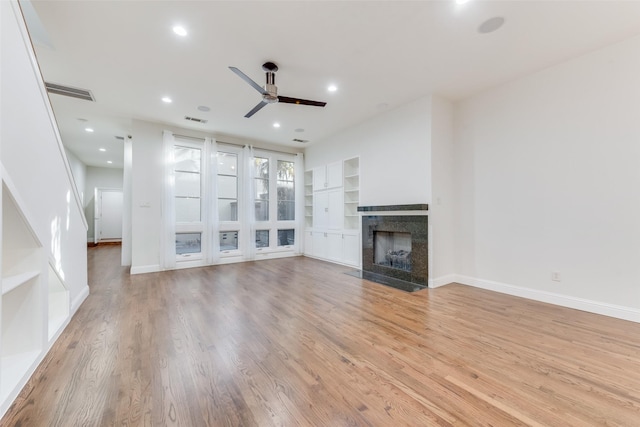 unfurnished living room with built in shelves, light hardwood / wood-style floors, and ceiling fan