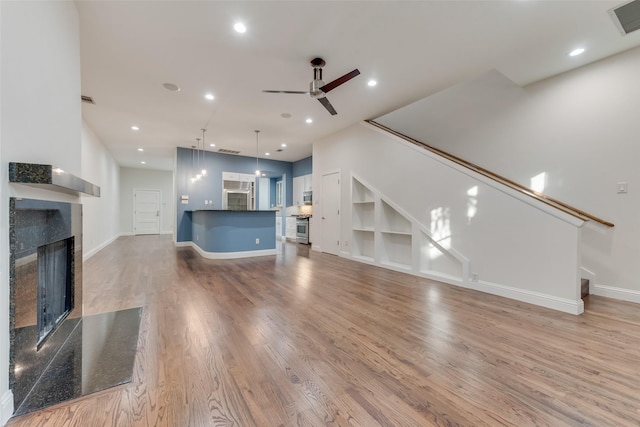 unfurnished living room with ceiling fan, built in shelves, a fireplace, and light hardwood / wood-style floors