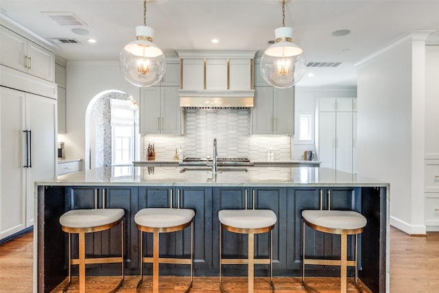 kitchen featuring decorative light fixtures, a large island with sink, and paneled built in refrigerator