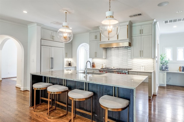 kitchen with sink, dark wood-type flooring, a spacious island, light stone countertops, and decorative backsplash