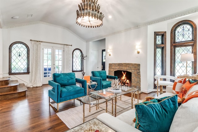 living room featuring french doors, a stone fireplace, vaulted ceiling, ornamental molding, and hardwood / wood-style floors