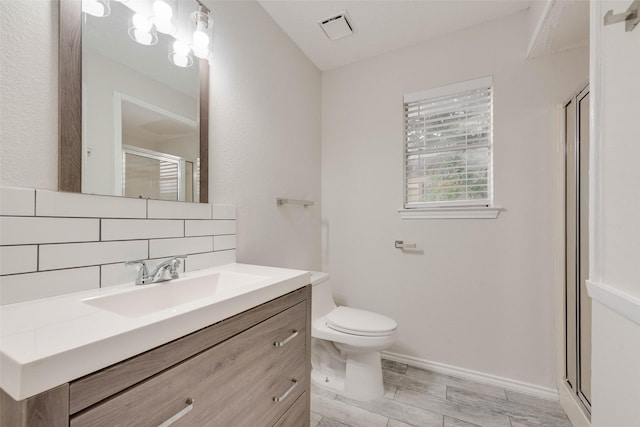 bathroom featuring vanity, backsplash, a shower with door, and toilet