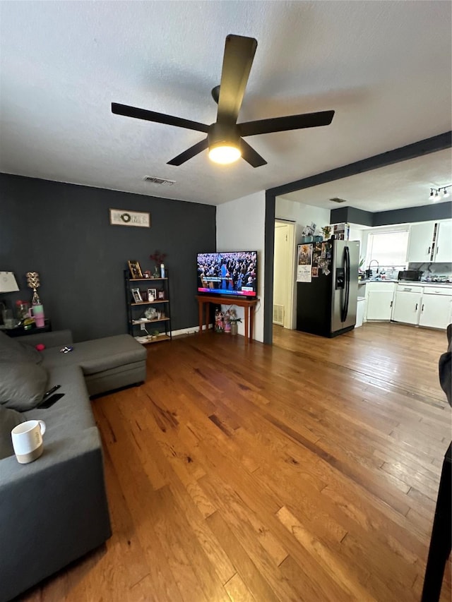 living room with a textured ceiling, ceiling fan, and light hardwood / wood-style flooring