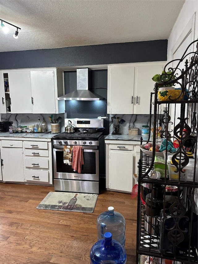 kitchen featuring white cabinets, wall chimney exhaust hood, wood-type flooring, and stainless steel gas stove