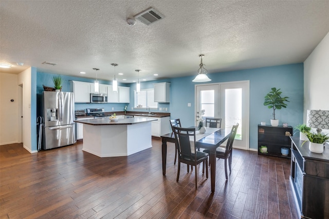 kitchen with stainless steel appliances, white cabinetry, a center island, and decorative light fixtures