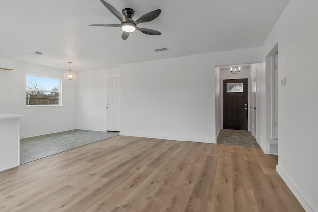 unfurnished living room with ceiling fan with notable chandelier and light hardwood / wood-style floors