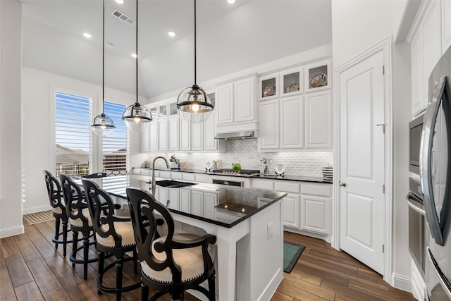 kitchen with decorative light fixtures, tasteful backsplash, white cabinets, a kitchen bar, and a kitchen island with sink