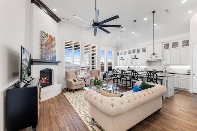 living room with ceiling fan, light hardwood / wood-style floors, a brick fireplace, and a towering ceiling