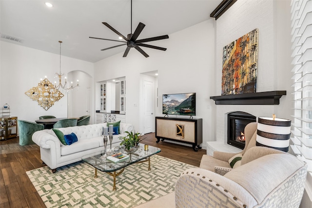 living room featuring dark hardwood / wood-style flooring, a brick fireplace, ceiling fan with notable chandelier, and a high ceiling