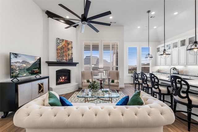 living room with a brick fireplace, hardwood / wood-style floors, sink, and ceiling fan