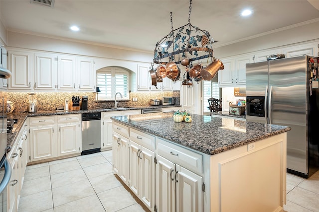 kitchen with a kitchen island, white cabinetry, dark stone countertops, ornamental molding, and stainless steel appliances