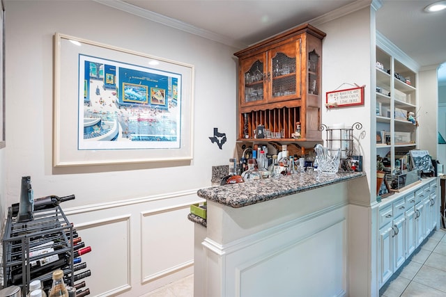 bar featuring ornamental molding, dark stone countertops, light tile patterned floors, and white cabinets