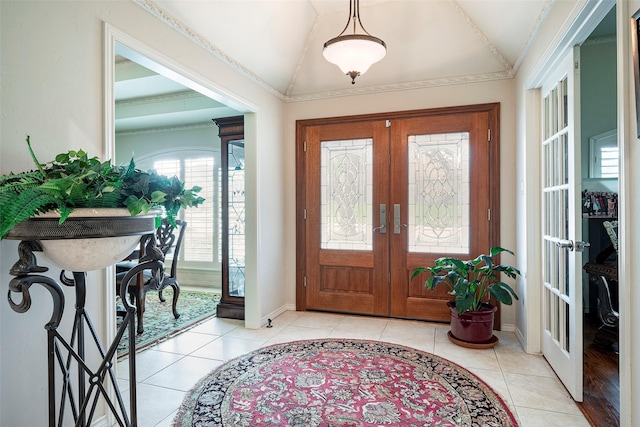 foyer entrance featuring french doors, ornamental molding, light tile patterned flooring, and vaulted ceiling