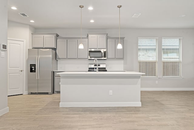 kitchen featuring gray cabinetry, decorative light fixtures, light hardwood / wood-style flooring, an island with sink, and stainless steel appliances