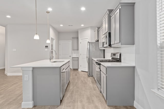 kitchen with sink, decorative light fixtures, a center island with sink, stainless steel appliances, and light hardwood / wood-style floors