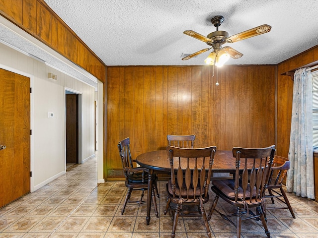 dining area with light tile patterned flooring, ceiling fan, wooden walls, and a textured ceiling