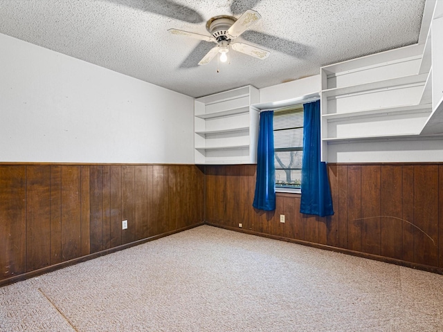 carpeted spare room with ceiling fan, a textured ceiling, and wood walls