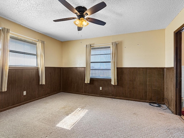 carpeted spare room with ceiling fan, wooden walls, and a textured ceiling