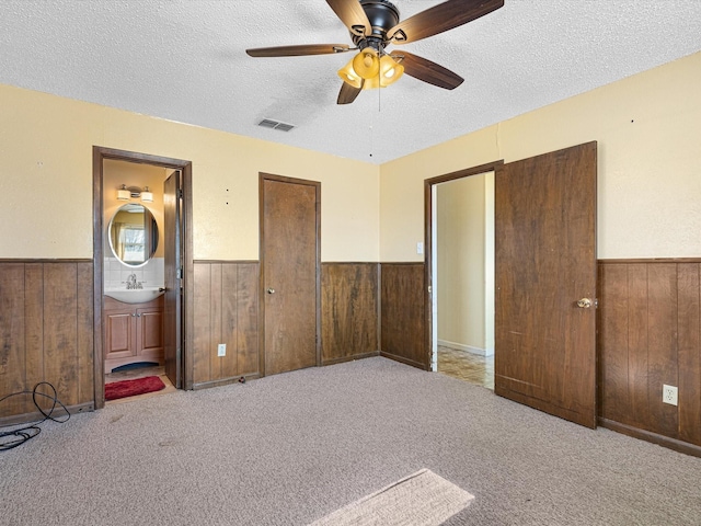 unfurnished bedroom with light colored carpet, wooden walls, sink, and a textured ceiling