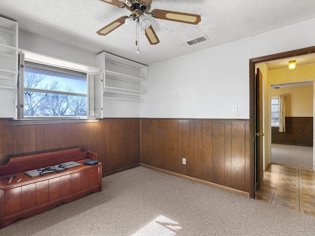 carpeted empty room featuring ceiling fan, a healthy amount of sunlight, a textured ceiling, and wood walls