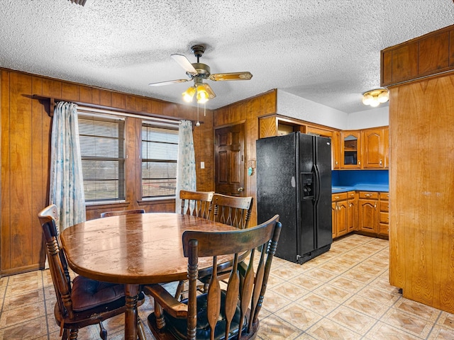 dining area with a textured ceiling, ceiling fan, and wood walls