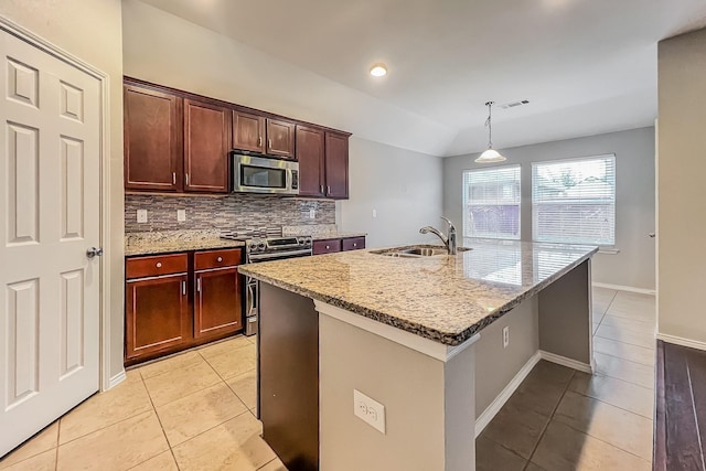 kitchen with sink, appliances with stainless steel finishes, light stone counters, an island with sink, and decorative light fixtures