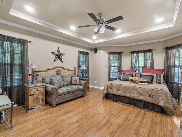 bedroom with a tray ceiling, multiple windows, and light wood-type flooring