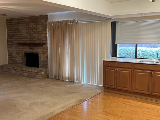 unfurnished living room featuring light carpet, a fireplace, a sink, and light wood-style floors