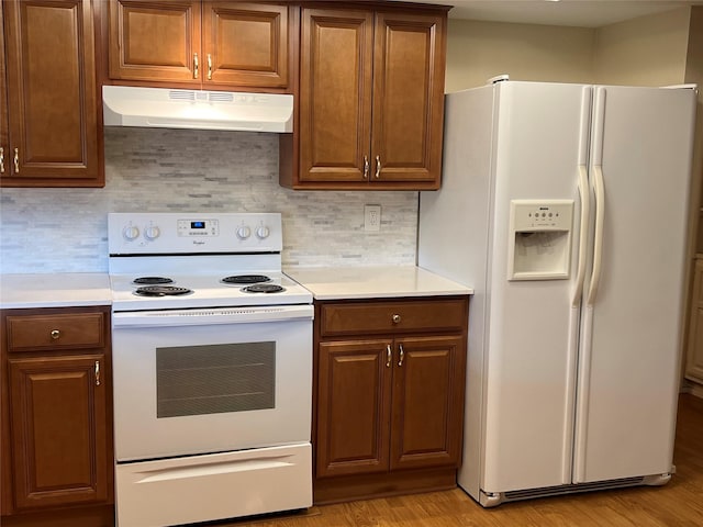 kitchen with white appliances, light countertops, under cabinet range hood, and backsplash