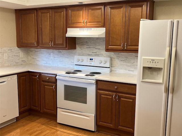 kitchen featuring light wood finished floors, light countertops, decorative backsplash, white appliances, and under cabinet range hood