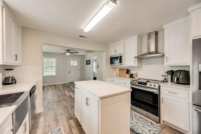 kitchen featuring white cabinetry, appliances with stainless steel finishes, a kitchen island, and wall chimney range hood