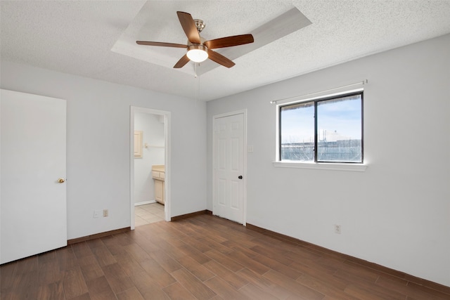 unfurnished bedroom featuring connected bathroom, dark wood-type flooring, a raised ceiling, and a textured ceiling