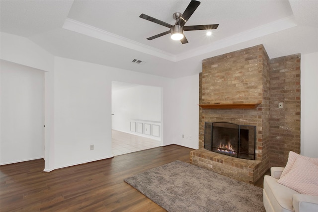 living room with hardwood / wood-style flooring, ceiling fan, a tray ceiling, a brick fireplace, and a textured ceiling