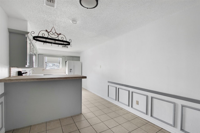 kitchen featuring gray cabinets, white refrigerator with ice dispenser, light tile patterned floors, and kitchen peninsula